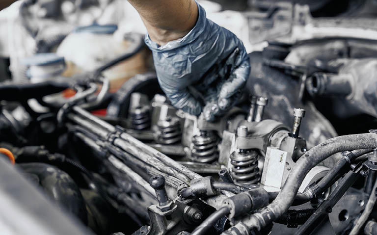 Close up of nozzles in car diesel engine with mechanic's hand in blue dirty rubber gloves doing professional auto repairing. Engine maintenance concept